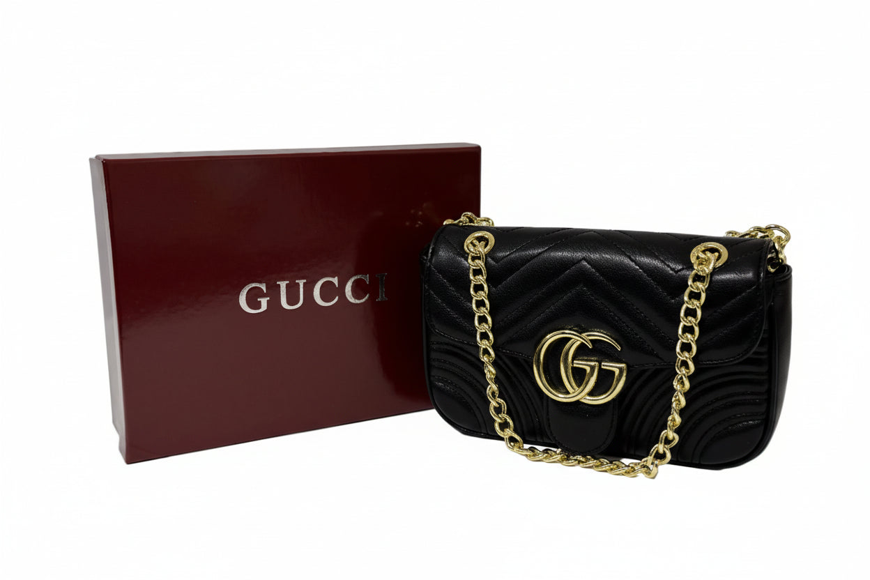 Black Gucci handbag with gold chain and matching box on a white surface.